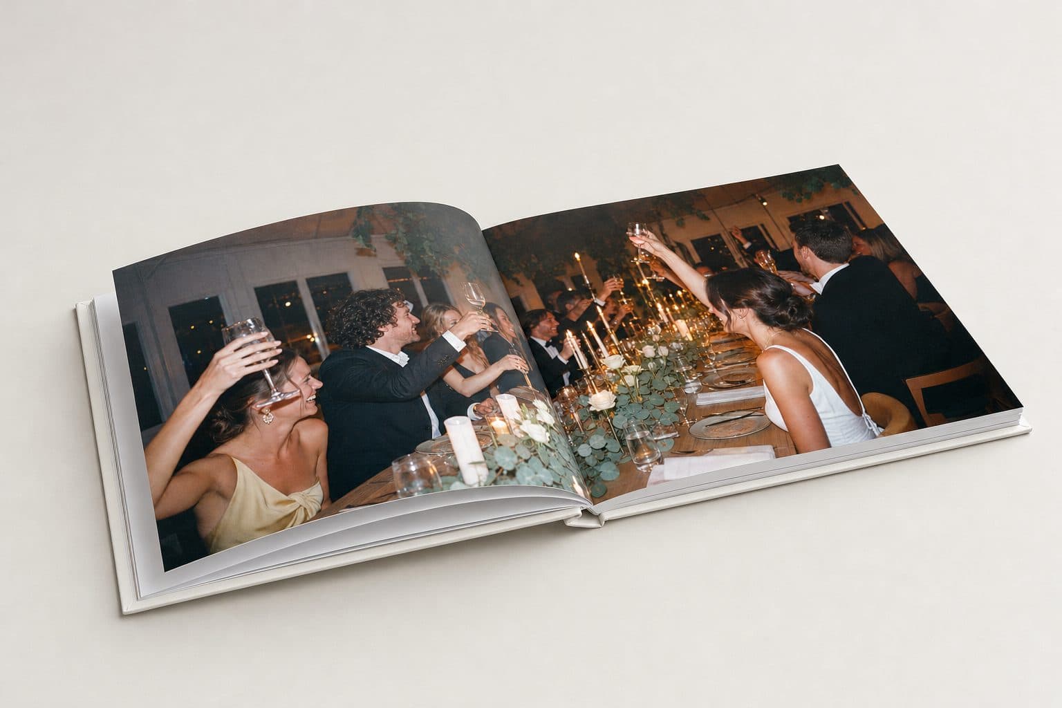 Aufgeblättertes Fotobuch mit einem Bild über die ganze Doppelseite: Gäste heben an der Kerzentafel die Gläser